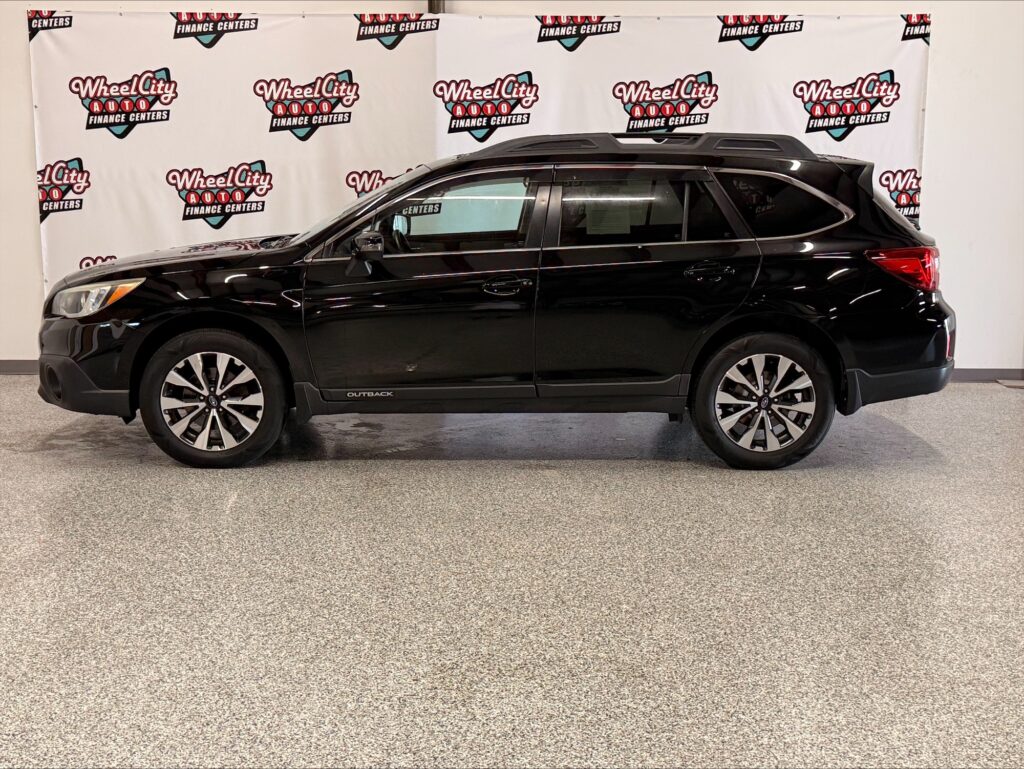 Side view of a black Subaru Outback SUV with roof rails, parked indoors against a Wheel City Auto Finance Centers backdrop.