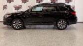 Side view of a black Subaru Outback SUV with roof rails, parked indoors against a Wheel City Auto Finance Centers backdrop.