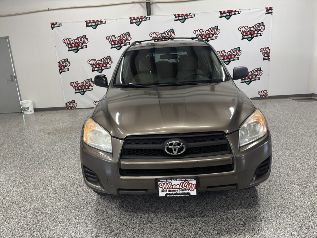 Front view of a tan Toyota SUV indoors, with a Wheel City Auto Finance Centers backdrop overhead.