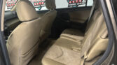 Beige car rear seat interior with headrests and seat belts, viewed from the open back door; logoed windows in the background.
