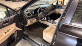 Inside a beige Subaru SUV with the driver’s door open, showing the steering wheel, dashboard, and front seats in a showroom.
