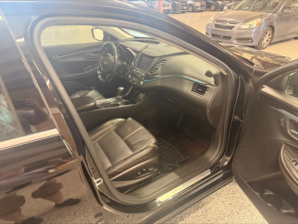 Interior of a dark leather car shown from the open driver’s side door with steering wheel and dashboard visible