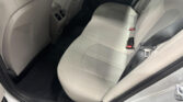 Rear car passenger seat area with light gray leather upholstery, center console air vents, and seat belts visible by the door.