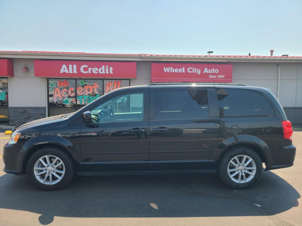 Front view of an auto shop with red storefront signs reading 'All Credit' and 'Wheel City Auto', a dark SUV parked in front.