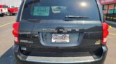 Rear view of a black Dodge Grand Caravan in a dealership lot, with a green D-1467 window sticker and Wheel City license plate frame.