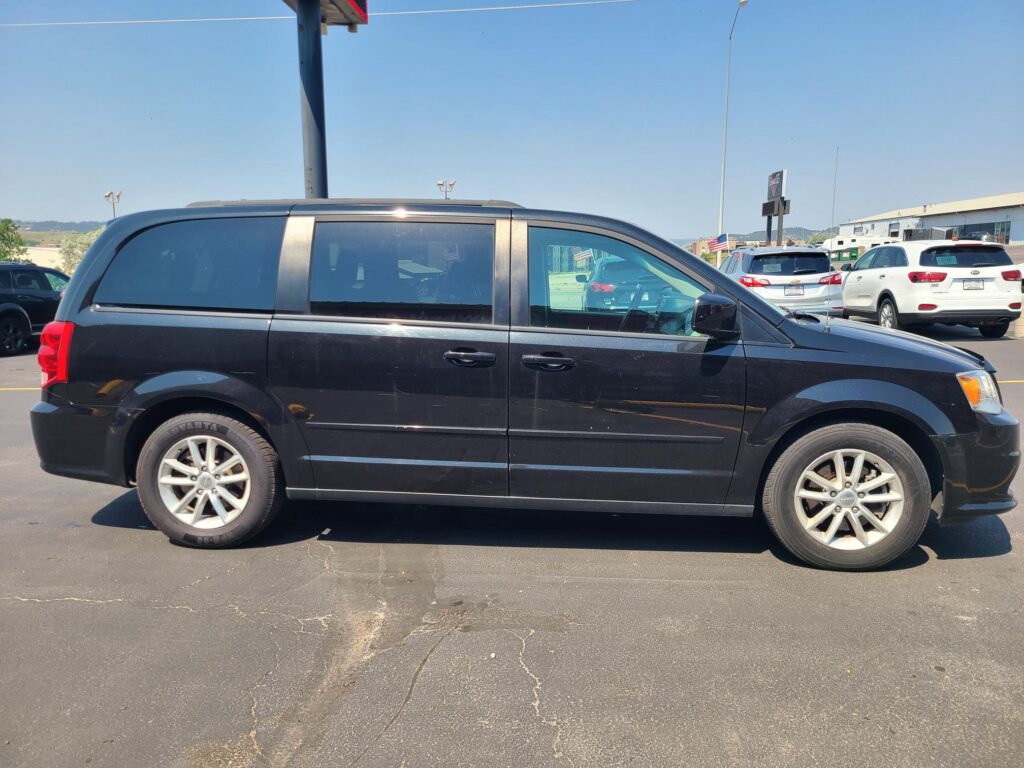 Side view of a black minivan in a parking lot with other cars and clear blue sky in the background.