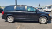 Side view of a black minivan in a parking lot with other cars and clear blue sky in the background.
