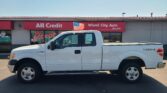 White pickup truck parked in front of a red All Credit Wheel City Auto sign with an American flag attached to the window.