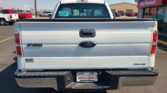 Rear view of a white Ford F-150 pickup in a dealership parking lot, with a Wheel City license plate frame visible in the bumper area.