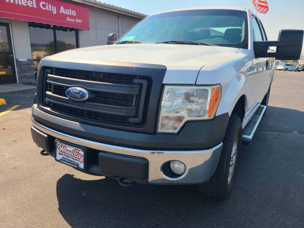 Front view of a white Ford cargo van parked at a dealership lot, showing the grille and headlights.