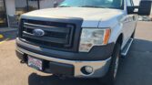 Front view of a white Ford cargo van parked at a dealership lot, showing the grille and headlights.