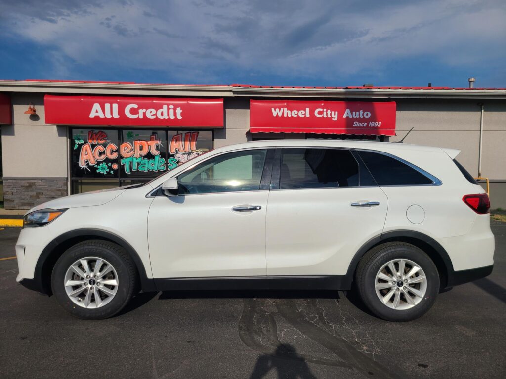 White SUV parked in front of a red storefront sign that reads 'All Credit Wheel City Auto'