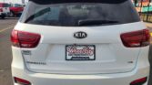 Rear view of a white Kia Sorento in a dealership lot; visible dealer plate frame and a window sticker showing D-1467, with a 'We Finance' sign in the background.