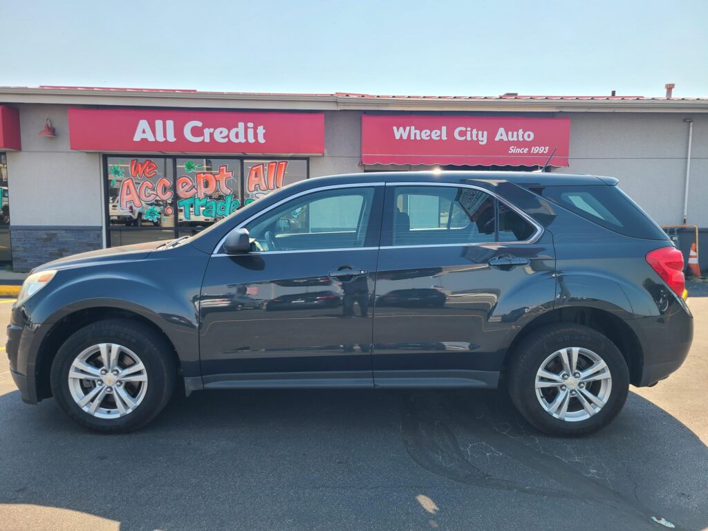 Blue SUV parked in front of an auto dealership with bright pink signs reading 'All Credit' and 'Wheel City Auto'