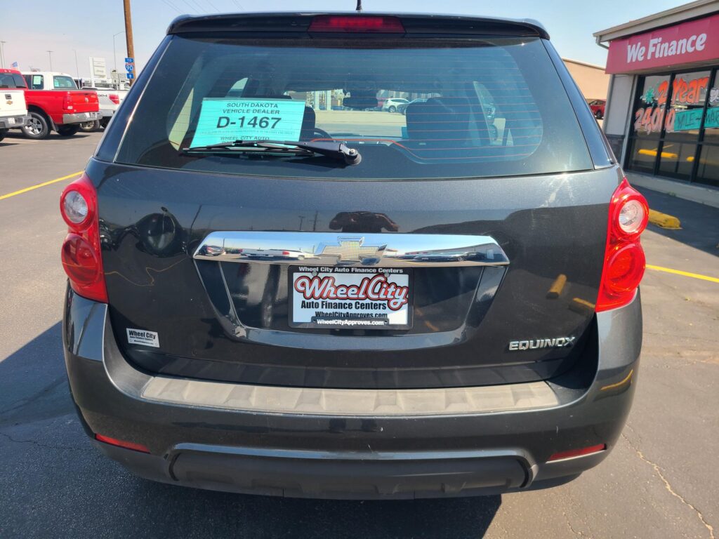 Rear view of a black Chevrolet Equinox in a dealership lot, with a teal D-1467 dealer sign on the rear window and Wheel City license plate frame.