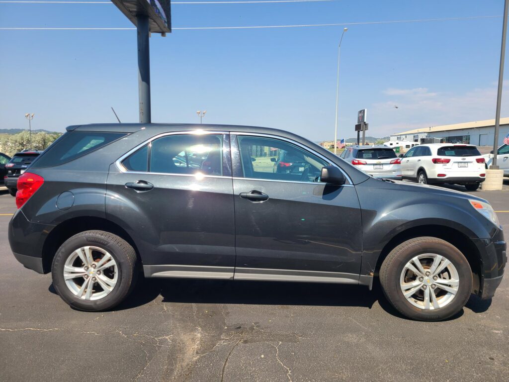 Side view of a dark gray SUV parked in a lot, with several white cars and a clear blue sky in the background.
