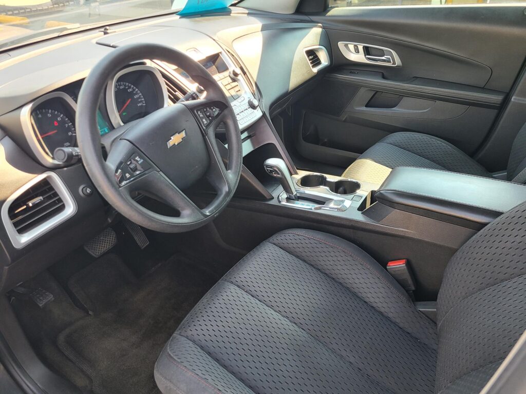 Interior of a Chevrolet sedan from the passenger side, showing the steering wheel, dashboard, center console, and front seats with black upholstery.