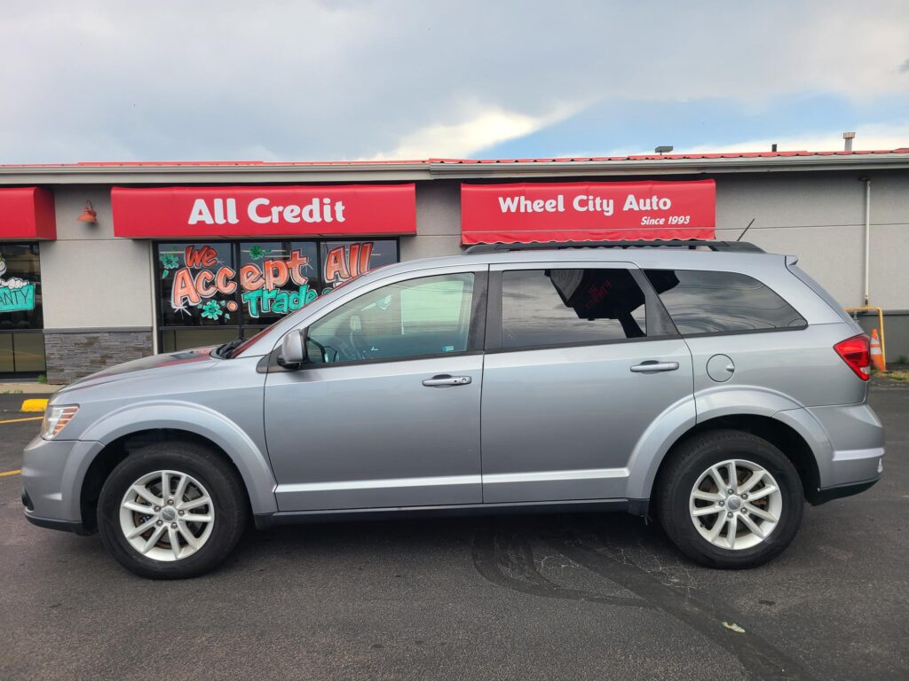 Silver SUV parked in front of a storefront with red signs reading 'All Credit' and 'Wheel City Auto'.