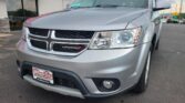 Silver Dodge minivan parked at a dealership, front view with Wheel City Auto license plate frame and red awning in the background