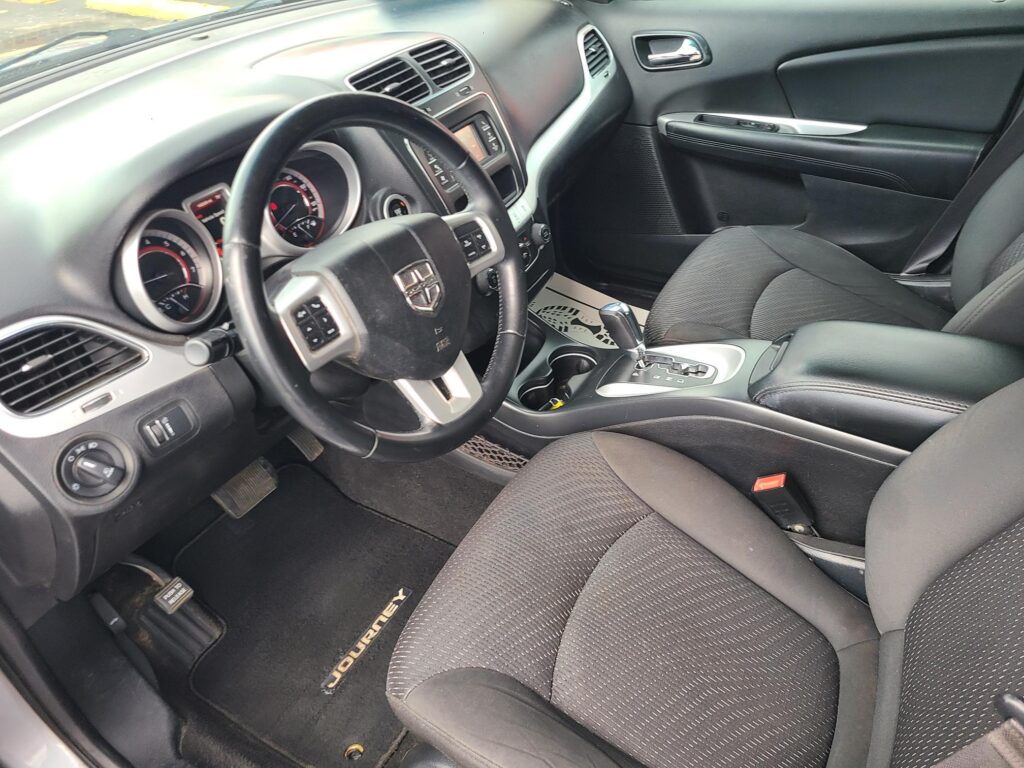 Driver's-side interior of a dark SUV, showing steering wheel with Dodge emblem, instrument cluster, and center stack.