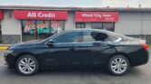 Black sedan parked in front of a car dealership with red signs reading All Credit and Wheel City Auto