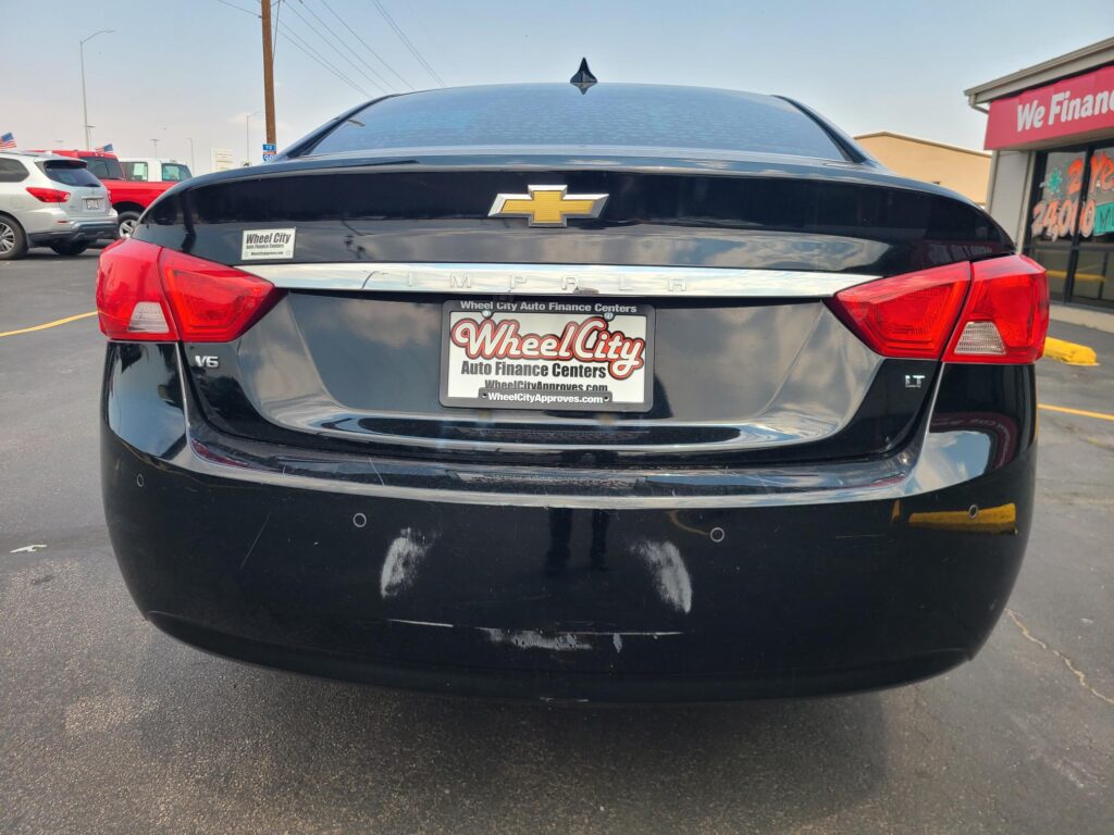 Rear of a black Chevrolet Impala with LT badge, showing Wheel City Auto Finance Centers license plate frame on a sunny parking lot.