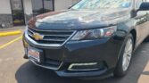 Front of a dark gray Chevrolet SUV parked in a lot with a red Wheel City Auto storefront sign in the background