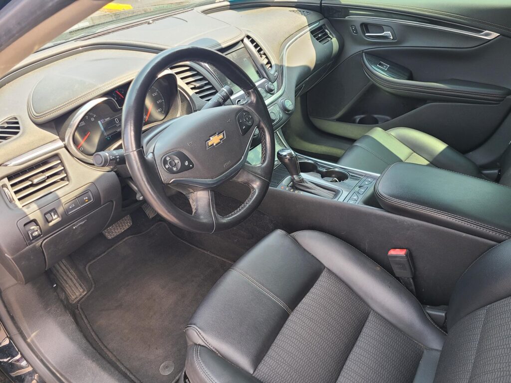 Front interior of a Chevrolet SUV: steering wheel with logo, dashboard, center console, and black leather seats.