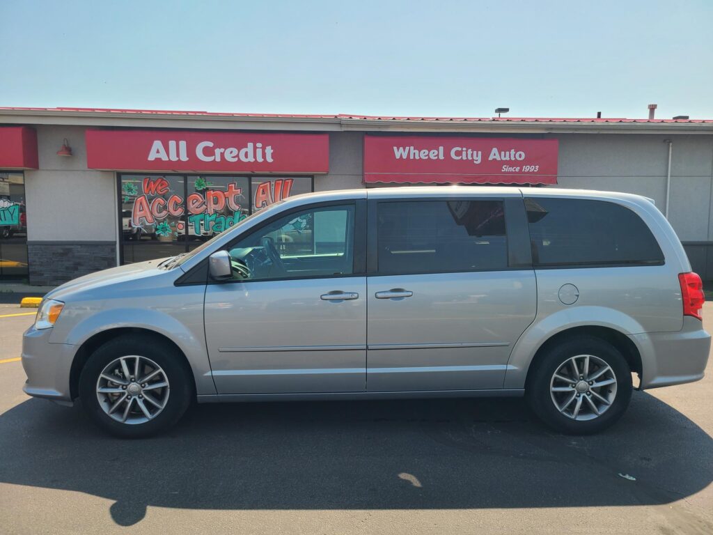 Silver minivan parked in front of a storefront with red All Credit and Wheel City Auto signs.