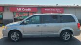 Silver minivan parked in front of a storefront with red All Credit and Wheel City Auto signs.