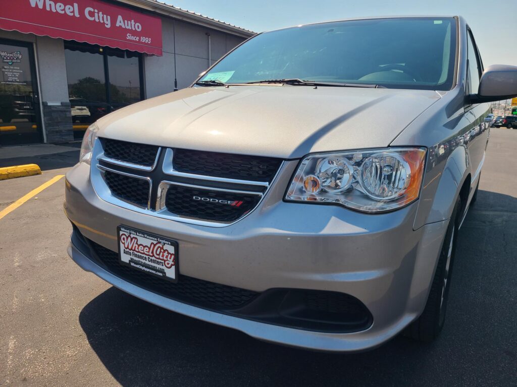 Close-up front view of a silver Dodge van parked in front of Wheel City Auto, with a red Wheel City sign above the storefront.