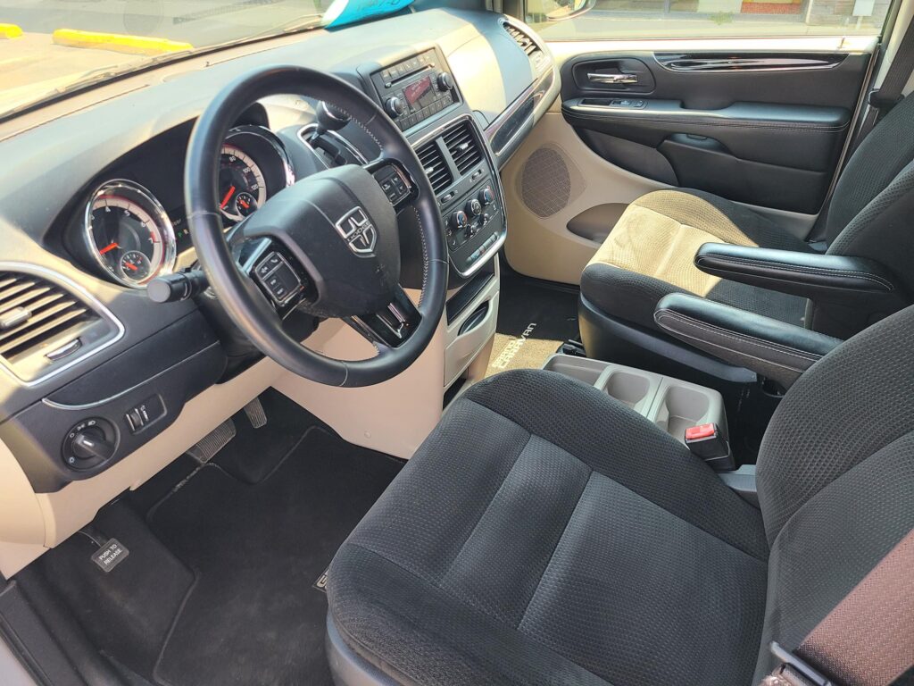 Front interior of a pickup/van cabin showing steering wheel, instrument cluster, center console, and passenger seat with dark fabric upholstery.