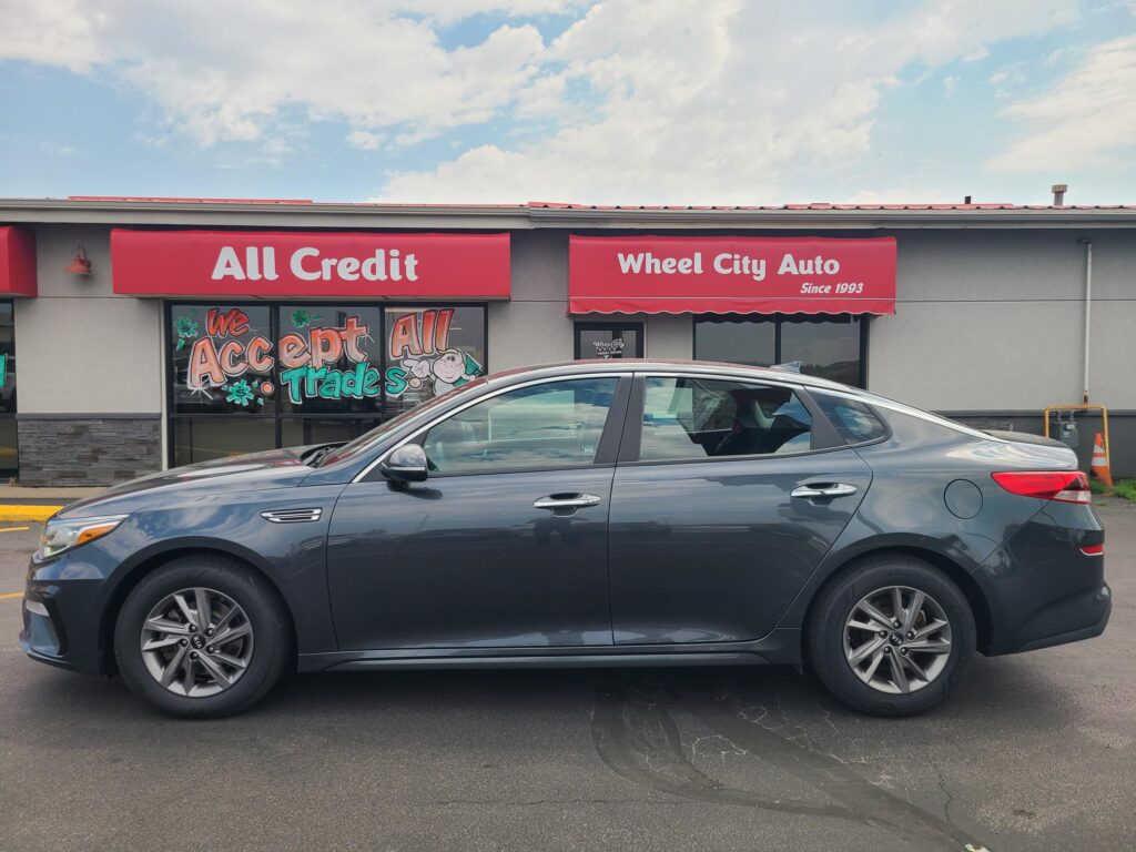 Front of All Credit Wheel City Auto dealership with red signs and a gray SUV parked in front.