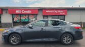 Front of All Credit Wheel City Auto dealership with red signs and a gray SUV parked in front.