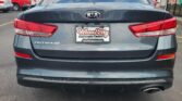 Rear view of a gray Kia Optima with a Wheel City Auto Finance Centers license plate frame in a dealership parking lot