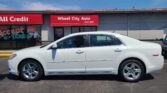 White sedan parked in front of a gray auto shop with a red Wheel City Auto awning and clear blue sky above.