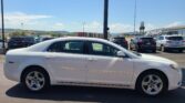 White sedan in the foreground of a crowded parking lot with other cars, a clear blue sky and distant hills.