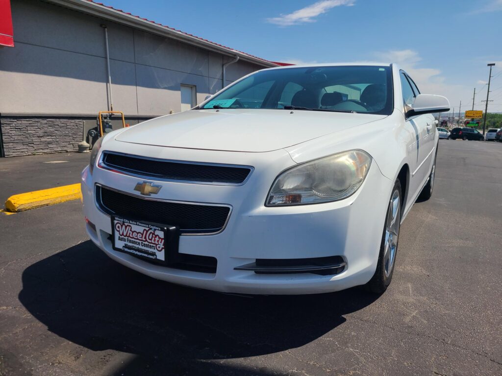 Front-left view of a white Chevrolet pickup in a parking lot, with a Wheel City Auto Finance Centers license plate frame visible.