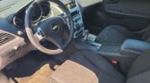 Interior of a Chevrolet car showing the steering wheel with the Chevy emblem, center console, and front seats viewed from the driver’s side.]","Driver’s cockpit with dashboard, air vents, and gear shifter in a dark fabric interior.