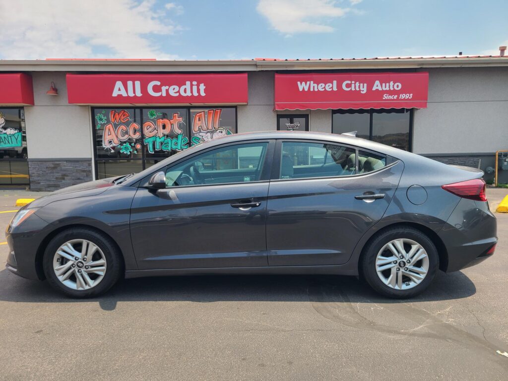Gray sedan parked in front of a storefront with red awnings that read 'All Credit' and 'Wheel City Auto'