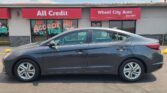 Gray sedan parked in front of a storefront with red awnings that read 'All Credit' and 'Wheel City Auto'