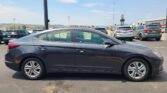 Gray Hyundai sedan in foreground in a crowded parking lot on a sunny day with other cars and American flags in the background.