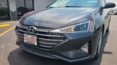 Front-left view of a gray Hyundai SUV parked in a dealership lot in front of Wheel City Auto with a red awning storefront.
