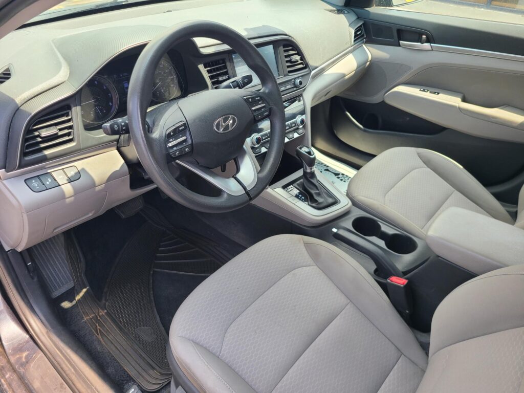 Interior of a car cabin showing the steering wheel, center console, gear shifter, and front seats viewed from the driver’s side.