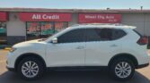 White SUV parked in front of a car dealership storefront with red 'All Credit' and 'Wheel City Auto' signs.