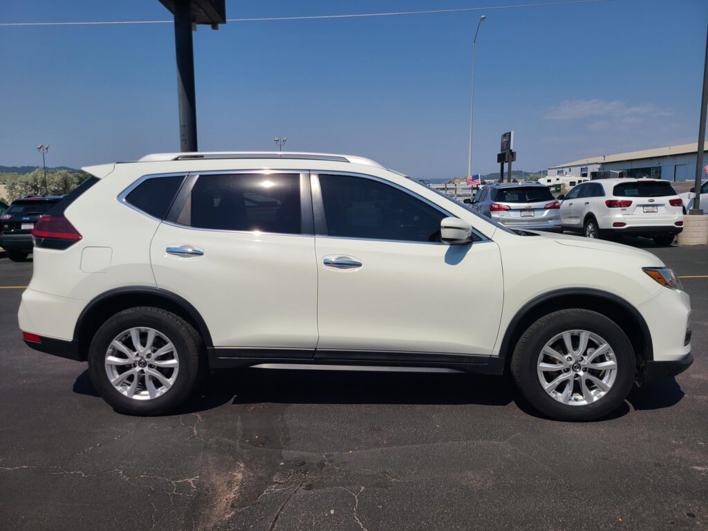 Side view of a white SUV parked in a lot with other cars and a building in the background, on a clear day.