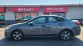 Gray sedan parked in a lot in front of a storefront with red signs reading All Credit and Wheel City Auto Auto Since 1993 .