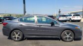 Side view of a dark gray sedan with alloy wheels in a crowded parking lot on a sunny day.