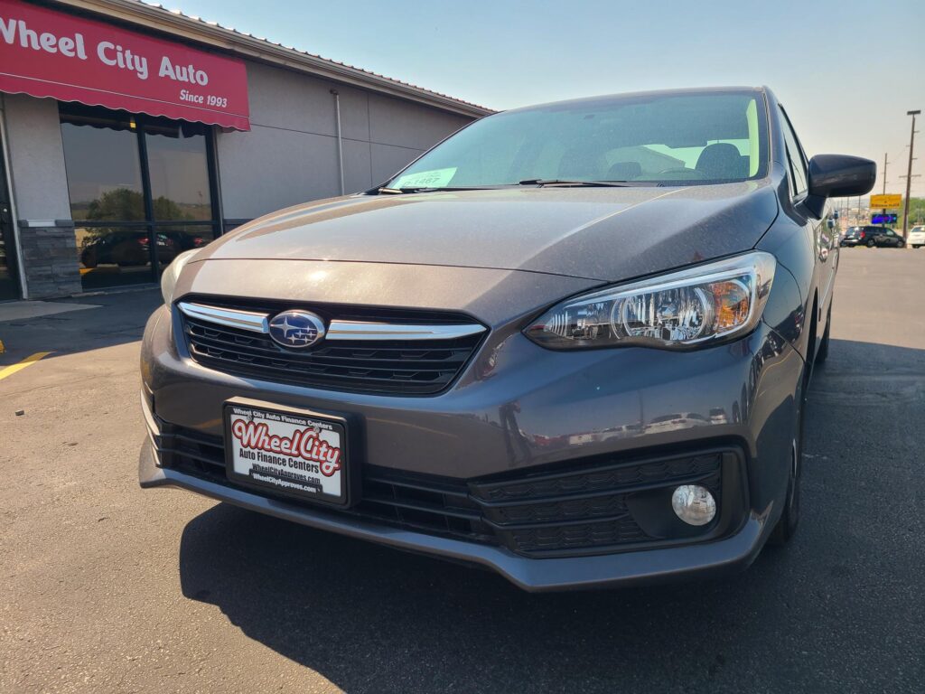Front-left view of a gray Subaru SUV in a car dealership lot with Wheel City Auto Finance Centers plate frame visible on the bumper