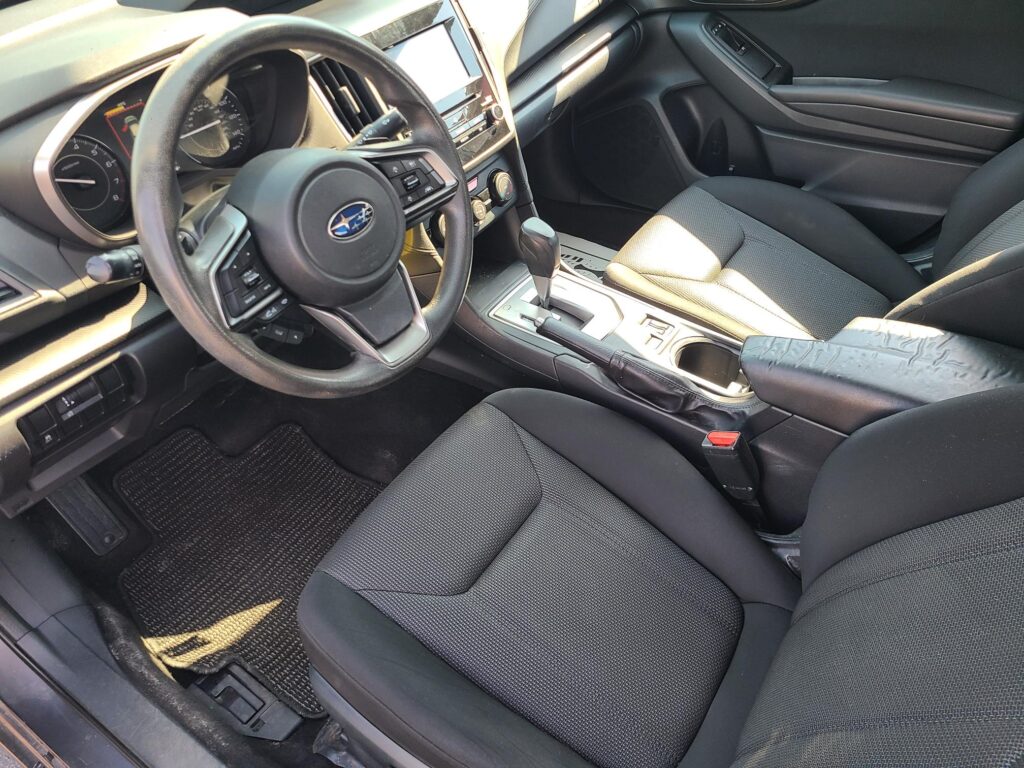 Dark fabric car interior with steering wheel on the left, dashboard gauges, center console, and touchscreen display visible between the seats